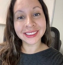 Smiling woman with nose ring and long brown hair wearing a gray top.